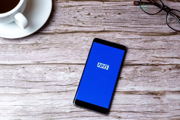 A phone on a table with the NHS logo on the screen